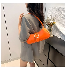 Model wearing a bright orange patent leather baguette bag over the shoulder with grey suit
