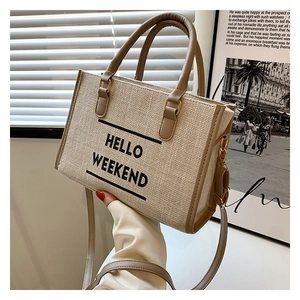 Detail of beige canvas tote bag with HELLO WEEKEND text and brown leather handles
