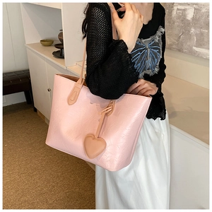 Detail of light pink tote bag with leather heart pendant worn on a shoulder