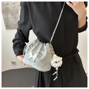 Detail of light gray bucket bag featuring a butterfly ornament and silver chain strap