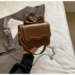 Detail of a brown vintage bow crossbody bag with wavy edges and metal chain strap