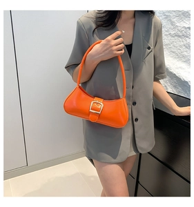 Detail of glossy orange leather underarm bag featuring a metallic silver square buckle