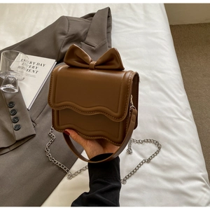 Close-up of brown PU leather crossbody bag featuring wavy edges and a decorative bow