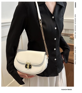 White saddle bag with gold chain strap shown on black striped shirt and white skirt