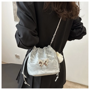 Silver pleated bucket bag with metal butterfly charm and plush ball on female model