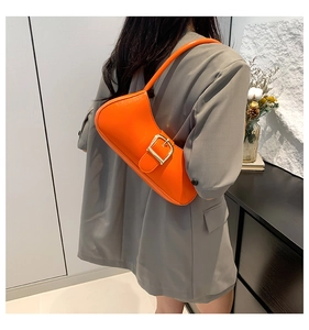 Detail of glossy orange patent leather shoulder bag with decorative large gold buckle