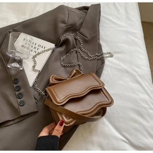 Detail of a brown leather crossbody bag with a stylish bow ornament and silver chain strap
