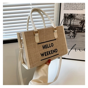 Close-up of beige woven tote bag featuring HELLO WEEKEND text and white leather handles