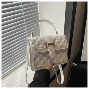 Detail of white quilted crossbody bag with a gold buckle and textured leather finish