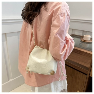 Detail of cream drawstring bucket bag with gold metal corners and chain strap