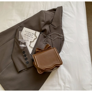 Close-up of a brown leather crossbody bag with a chic bow detail and scalloped bottom edge