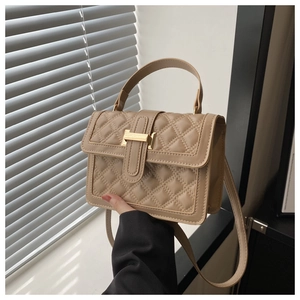 Detailed view of beige quilted handbag with gold metal bar and adjustable strap