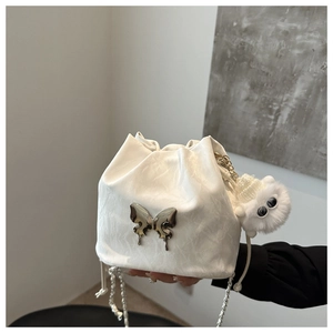 Detail of white drawstring bucket bag with silver butterfly buckle and pearl chain