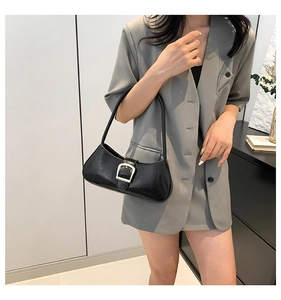Detail of minimalist black baguette bag with silver buckle worn with a grey blazer