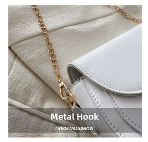 Detail shot of the golden hardware hook and chain on a white leather shoulder bag