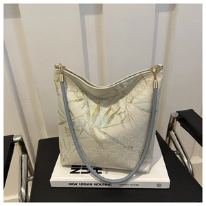 Nahaufnahme der goldenen Bambus-Stickerei auf dem cremeweißen Stoff der Handtasche