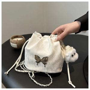 White bucket bag with silver butterfly charm and chain strap held by hand closeup