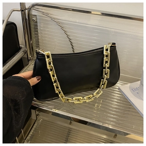 Détail d'un sac baguette en similicuir noir avec une grosse poignée en chaîne dorée