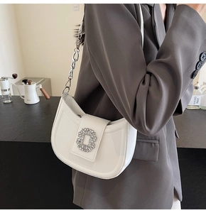 Detail of white leather hobo bag with crystal buckle and silver chain on model