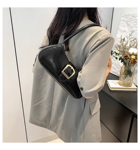 Detail of black glossy hobo bag with gold buckle worn over a grey blazer