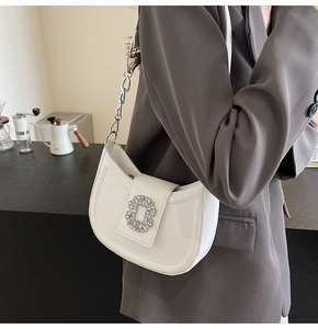 Close-up of elegant cream-colored crescent shoulder bag with silver rhinestone buckle detail