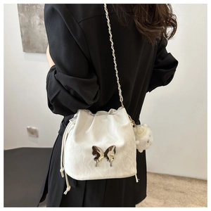Detail of white drawstring bucket bag featuring a silver metal butterfly and plush pompom