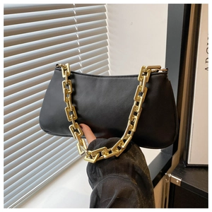 Detail of matte black leather handbag with chunky gold square chain strap on shoulder