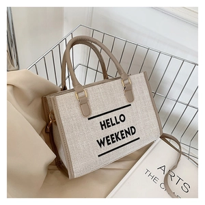 Detail of canvas tote bag with Hello Weekend print and brown leather handles in a wire basket