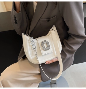 Detail of off-white hobo bag with rhinestone buckle and silver chain on model