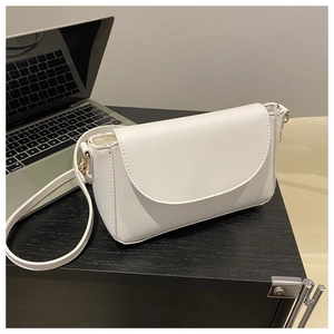White minimalist leather crossbody bag with gold buckle on a desk with laptop background