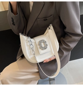Close-up of a white half-moon shoulder bag with a sparkling rhinestone buckle and silver chain
