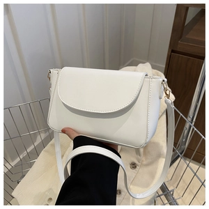Close-up of white crossbody bag featuring a curved flap and gold metal hardware detail