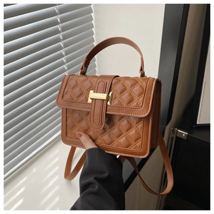 Detail of brown quilted crossbody bag with yellow stitching and gold H-shaped clasp