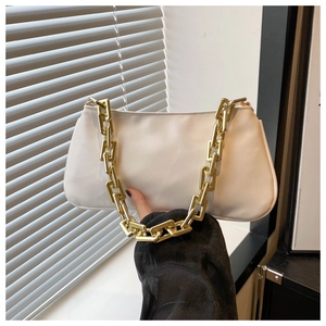 Detail of white leather baguette bag featuring chunky gold chain strap held by model