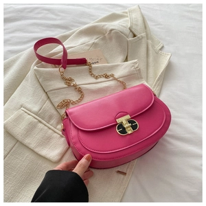 Detail of magenta saddle bag featuring a gold twist lock and metal chain strap