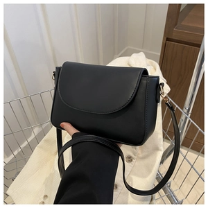 Detail of a minimalist black matte leather crossbody bag resting in a shopping cart