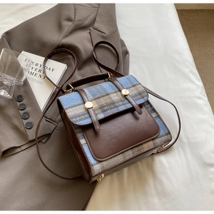 Detail of British style plaid backpack with leather flap and golden buckle on white bedding