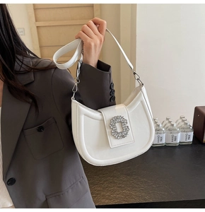 Close-up of a white leather crescent bag featuring a crystal buckle on the shoulder