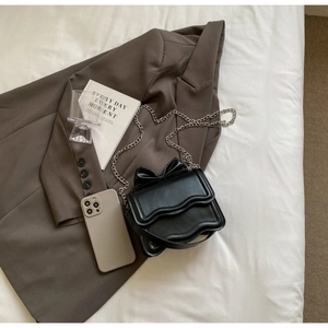 Detail of black PU leather crossbody bag with top bow and wave-cut edge design