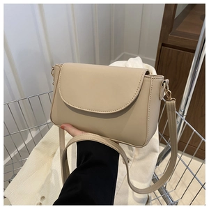 Detail of a beige faux leather crossbody bag with a curved flap and gold metal hardware