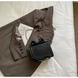 Detail of black crossbody bag featuring a leather bow and wavy edge design on suit