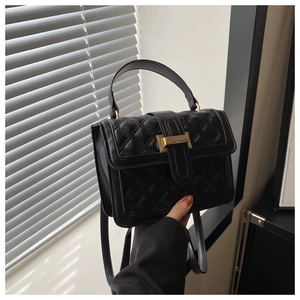 Detail of black quilted cross-body bag featuring a gold metal clasp and leather handle