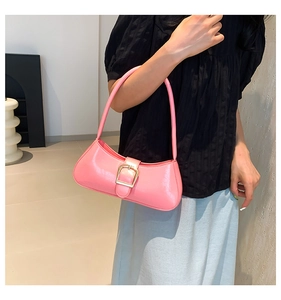 Detail of pink patent leather baguette bag with a gold buckle worn on the shoulder