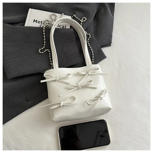 Detail view of cream white bow handbag with silver bead chain and smartphone for scale