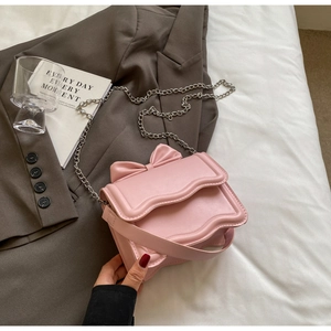 Pink crossbody bag with large bow detail and wavy flap on a stylish suit jacket