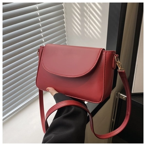 Detail of red minimalist flap shoulder bag with smooth leather texture and adjustable strap