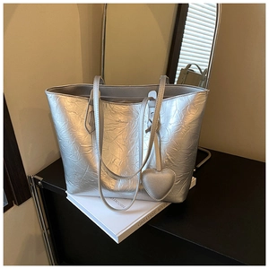 Silver wrinkled leather tote bag with a heart charm displayed on decorative books