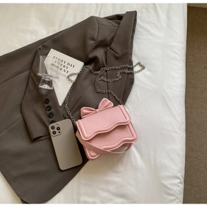 Pink leather chain bag with decorative bow and wavy flap edges on white fabric