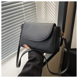 Close-up of black leather crossbody bag with curved flap and gold metal hardware hooks