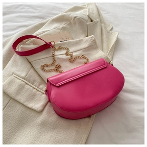 Macro shot of a magenta saddle bag on a white blazer with gold chain detail